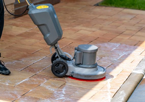 chemical machine cleaning concrete pavement in front of the house with a brush